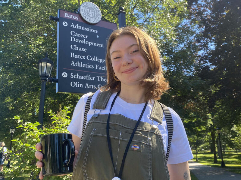 A woman wearing overalls standing outside in a park. 