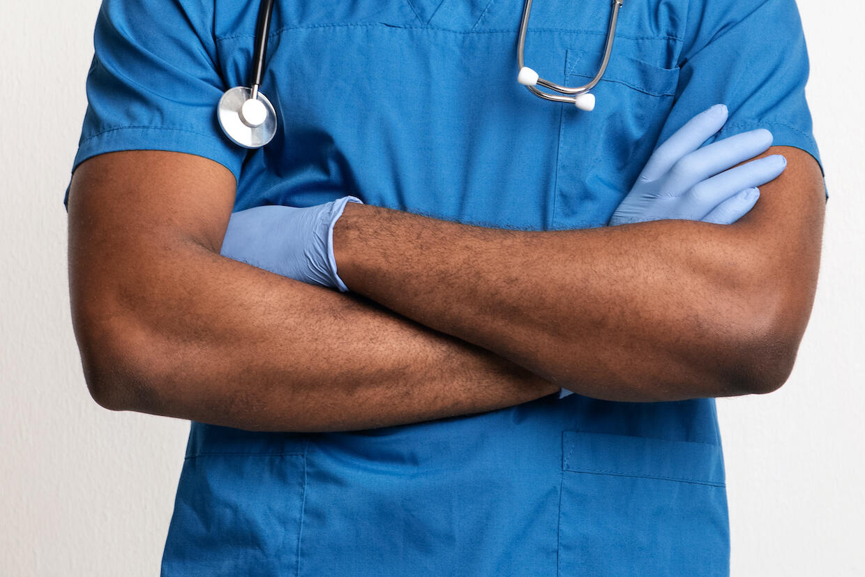 A person in medical scrubs and a stethoscope standing with their arms crossed.