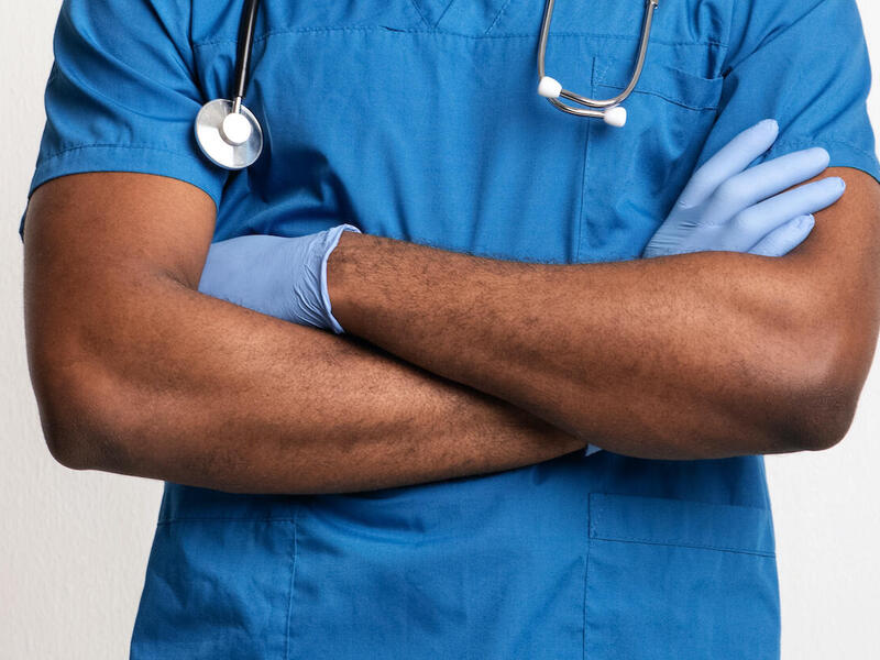 A person in medical scrubs and a stethoscope standing with their arms crossed.
