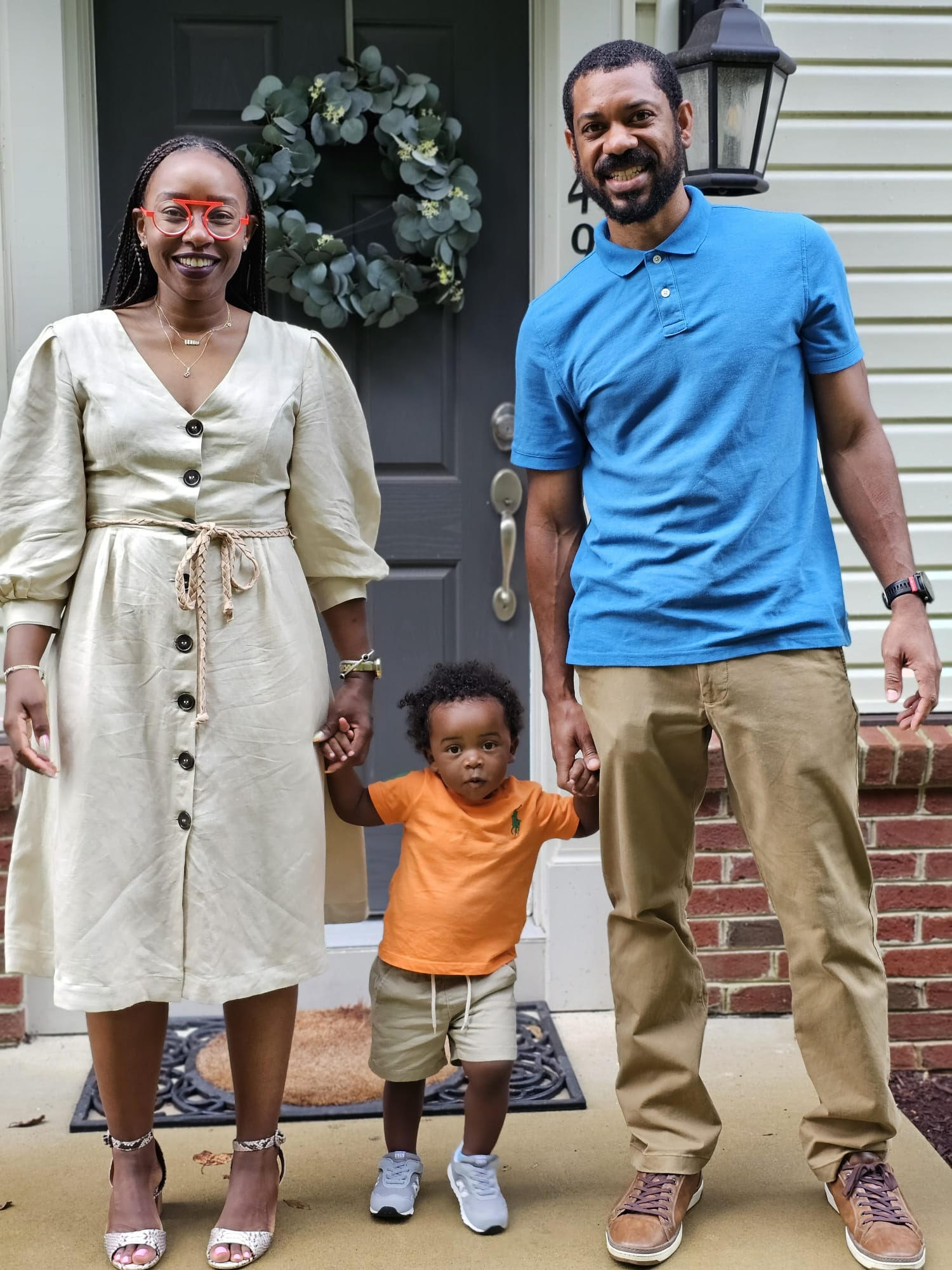 A photo of a man and a woman on either side of a toddler and holding his hands. 