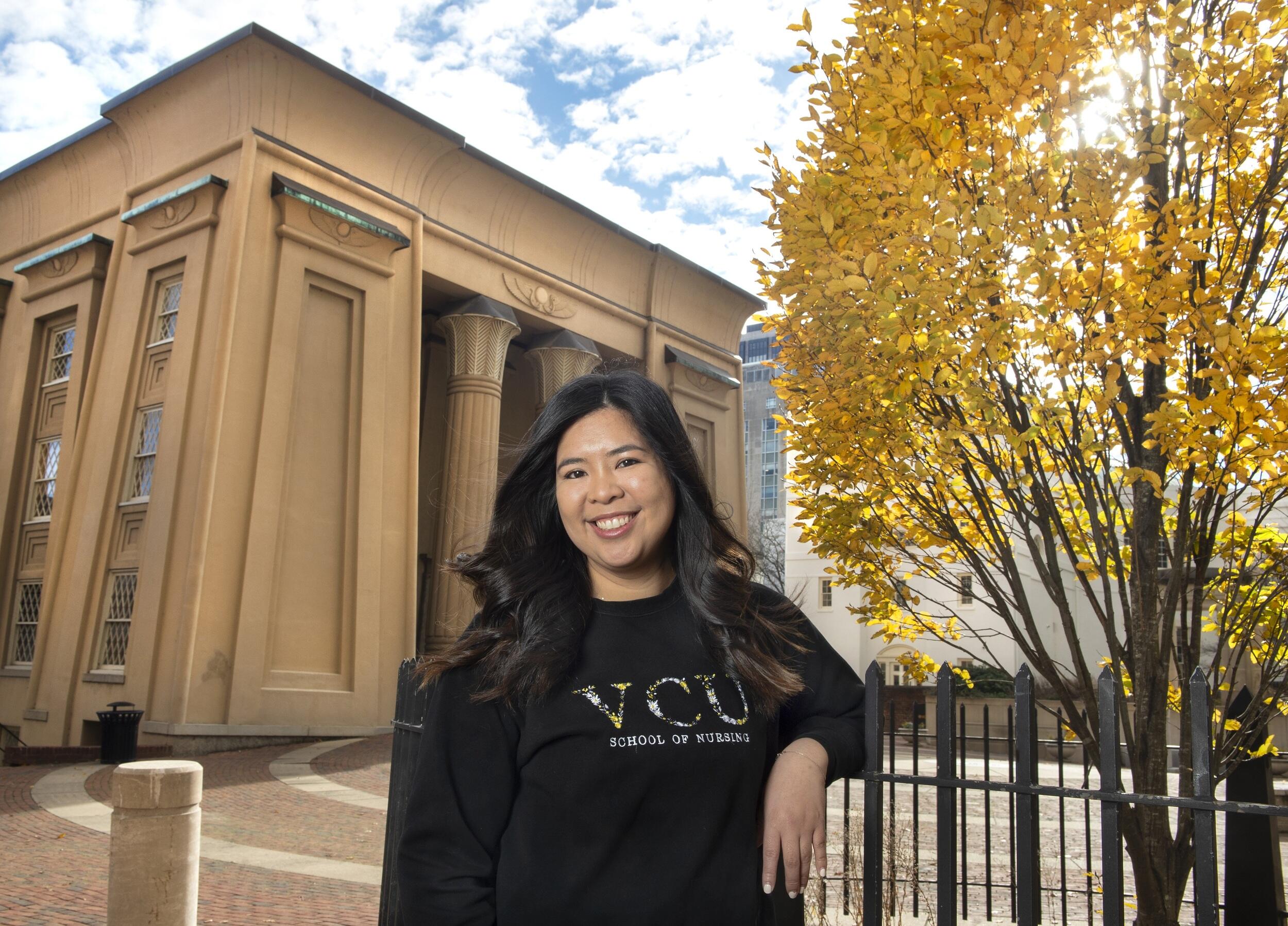 A photo of a woman standing outside leaning against a fence. 