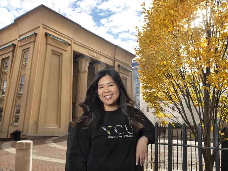 A photo of a woman standing outside leaning against a fence. 
