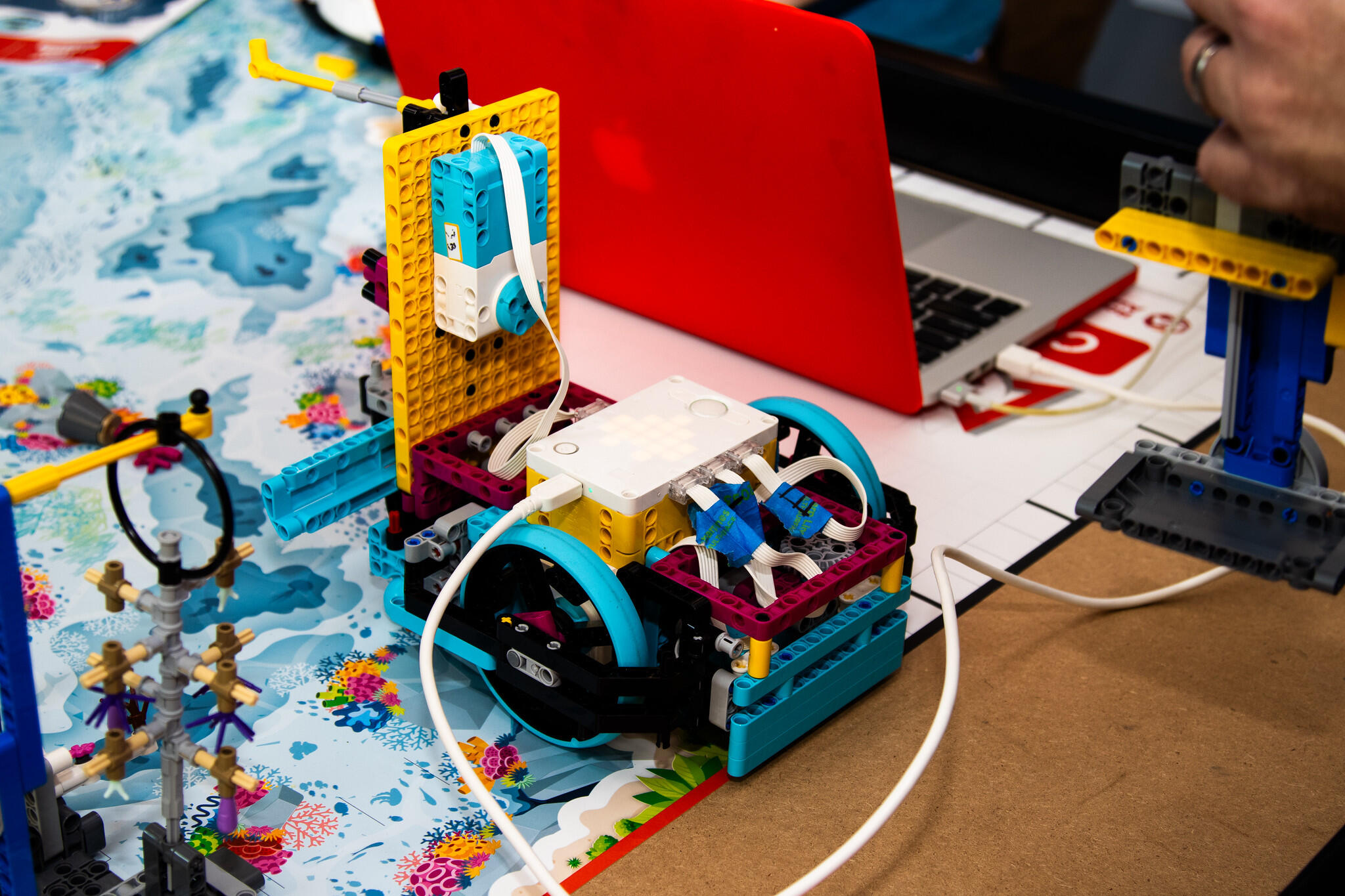 A photo of a robot build out of legos with wires that are hooked up to a laptop. 