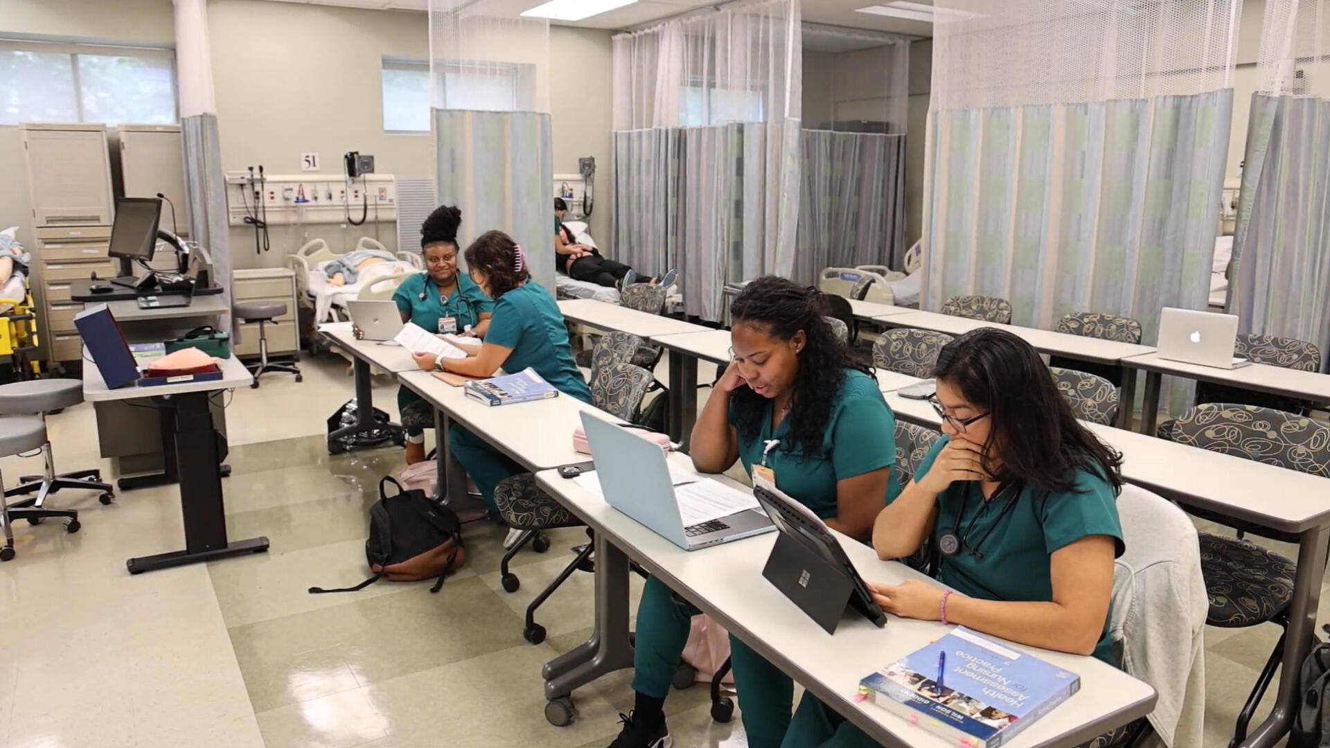 A photo of pour people in blue nurse scrubs sitting at a long table. 