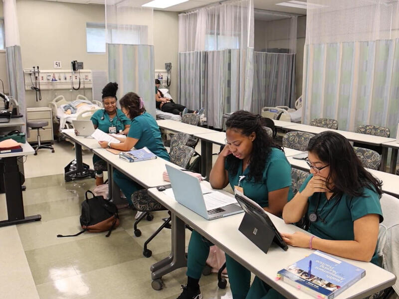 A photo of pour people in blue nurse scrubs sitting at a long table. 