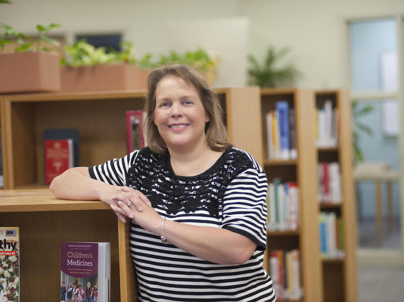 Woman leans and smiles on library bookshelf. 