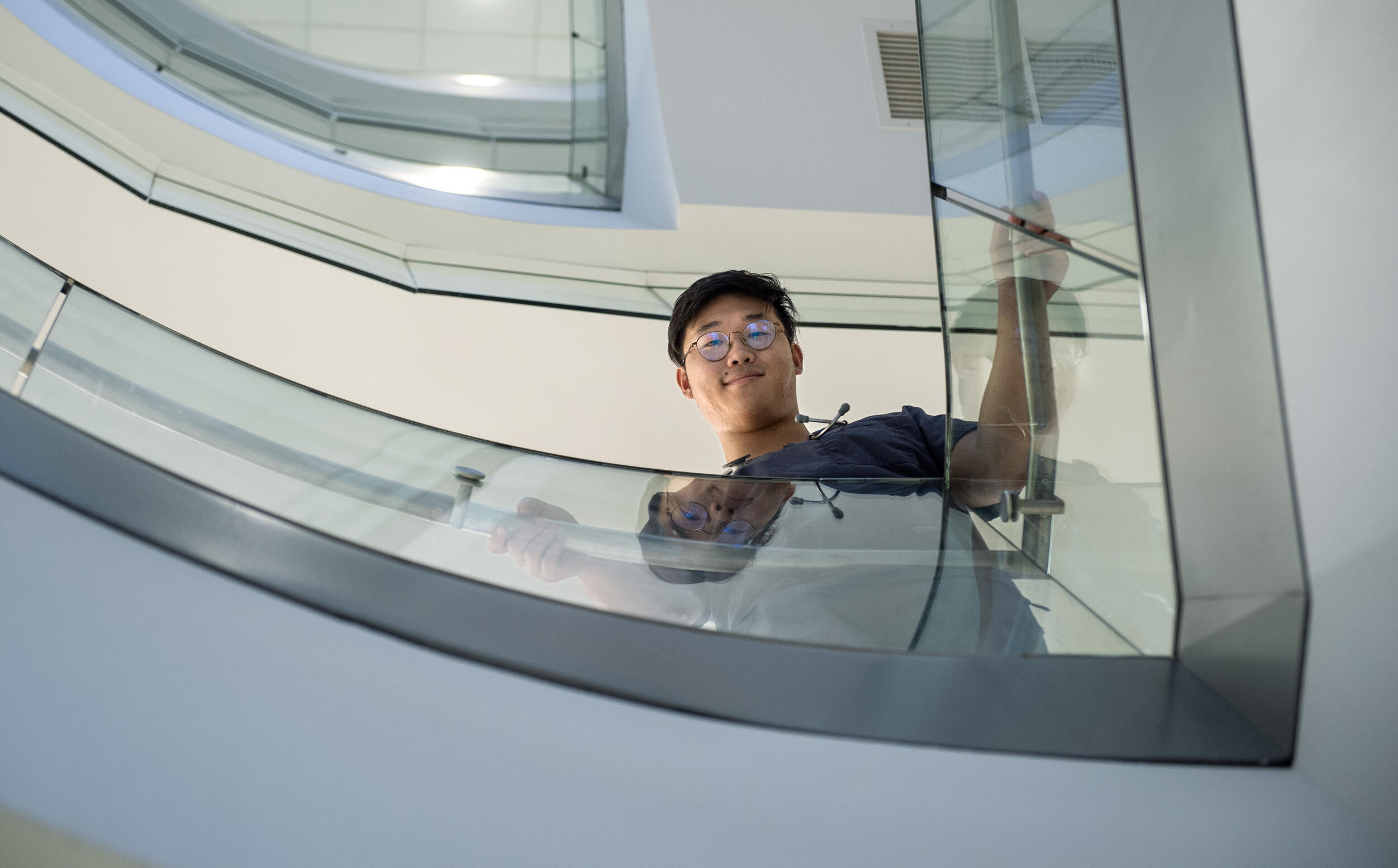 A photo of a man looking down from a stairwell with glass railing. 