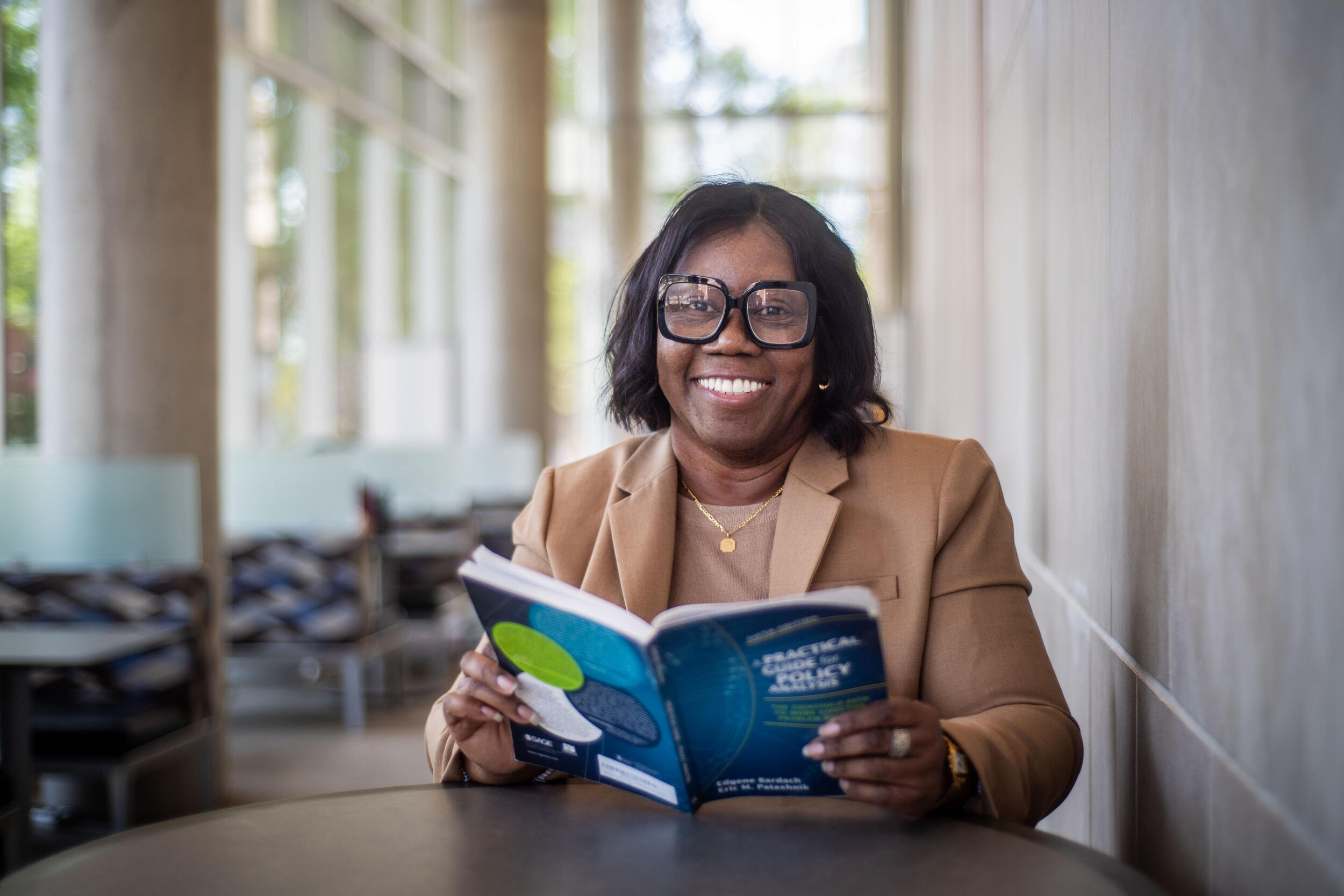A photo of a woman sittng at a table and reading a book. 