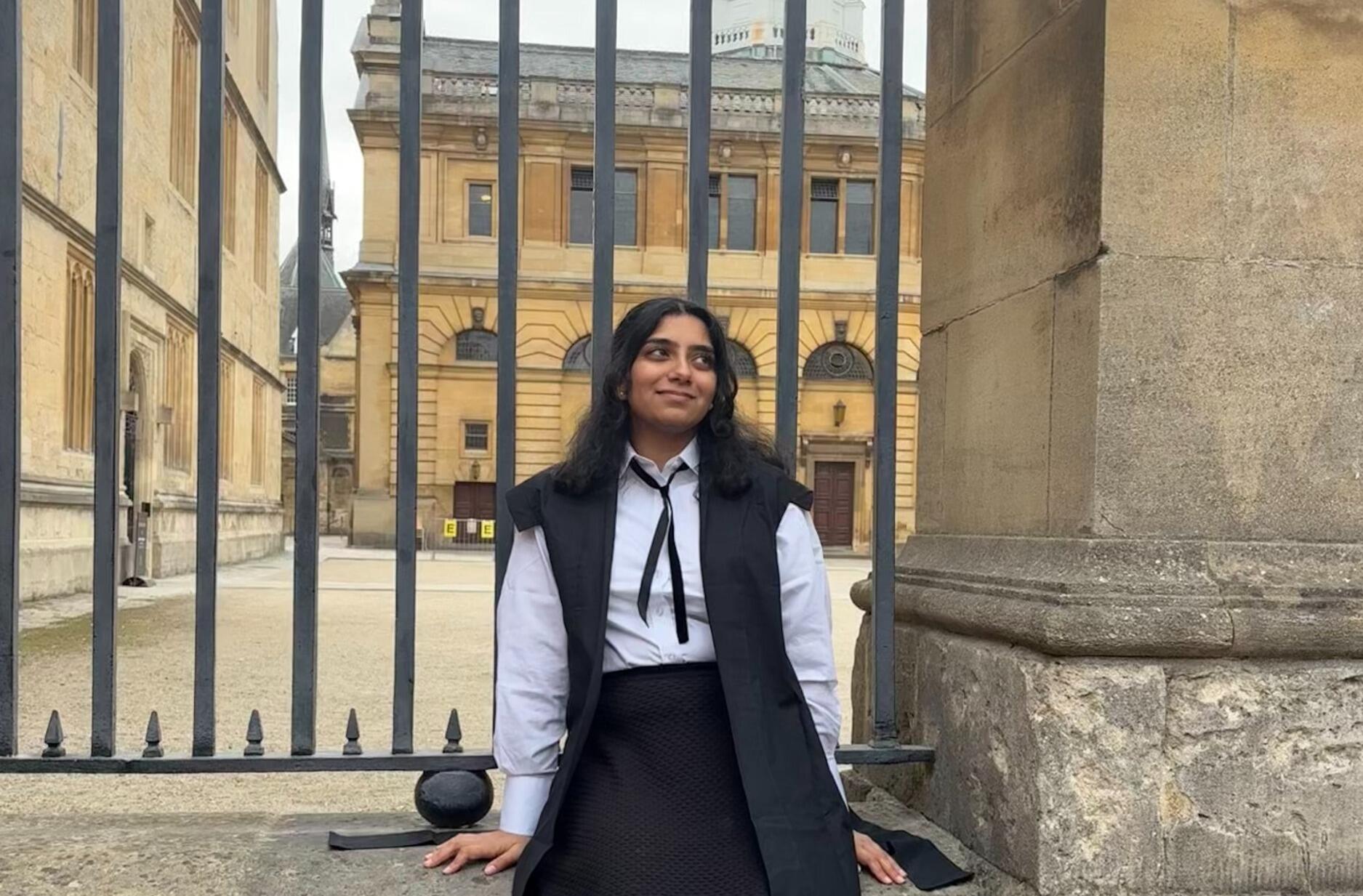 A photo of a woman sitting in front of a gate. 