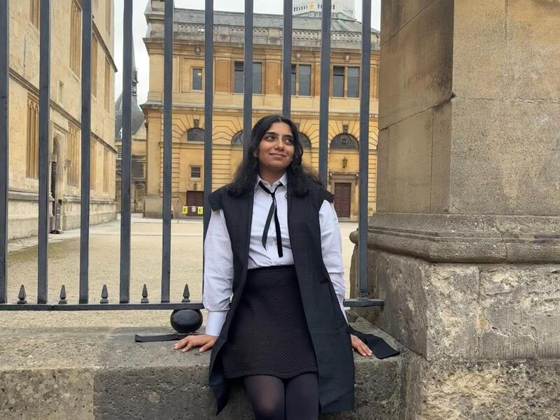 A photo of a woman sitting in front of a gate. 