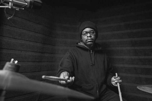 A drummer sits at a drum set in a recording studio.