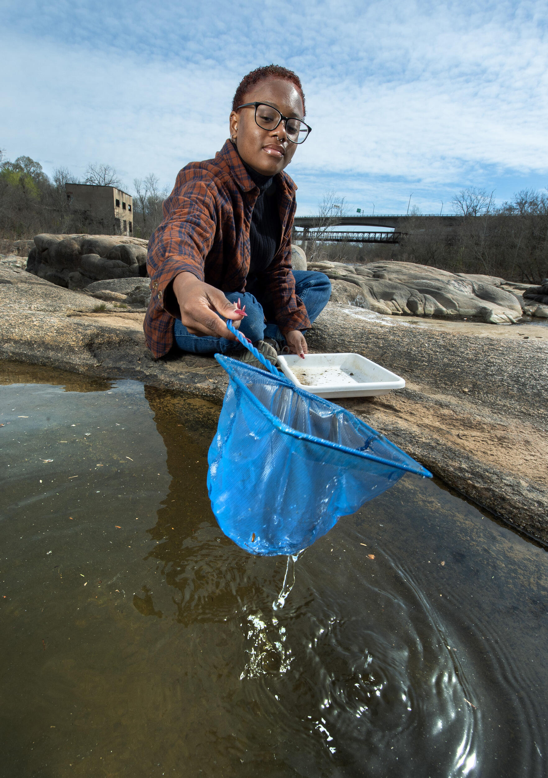 A photo of a person holding a blue net over a rock pool. 