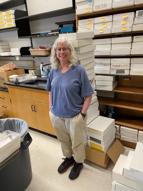 A photo of a woman standing in a room with shelves full of white boxes. 