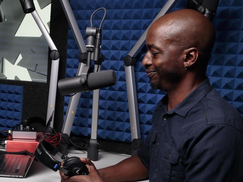 A photo of a man in front of a microphone in a recording studio. 