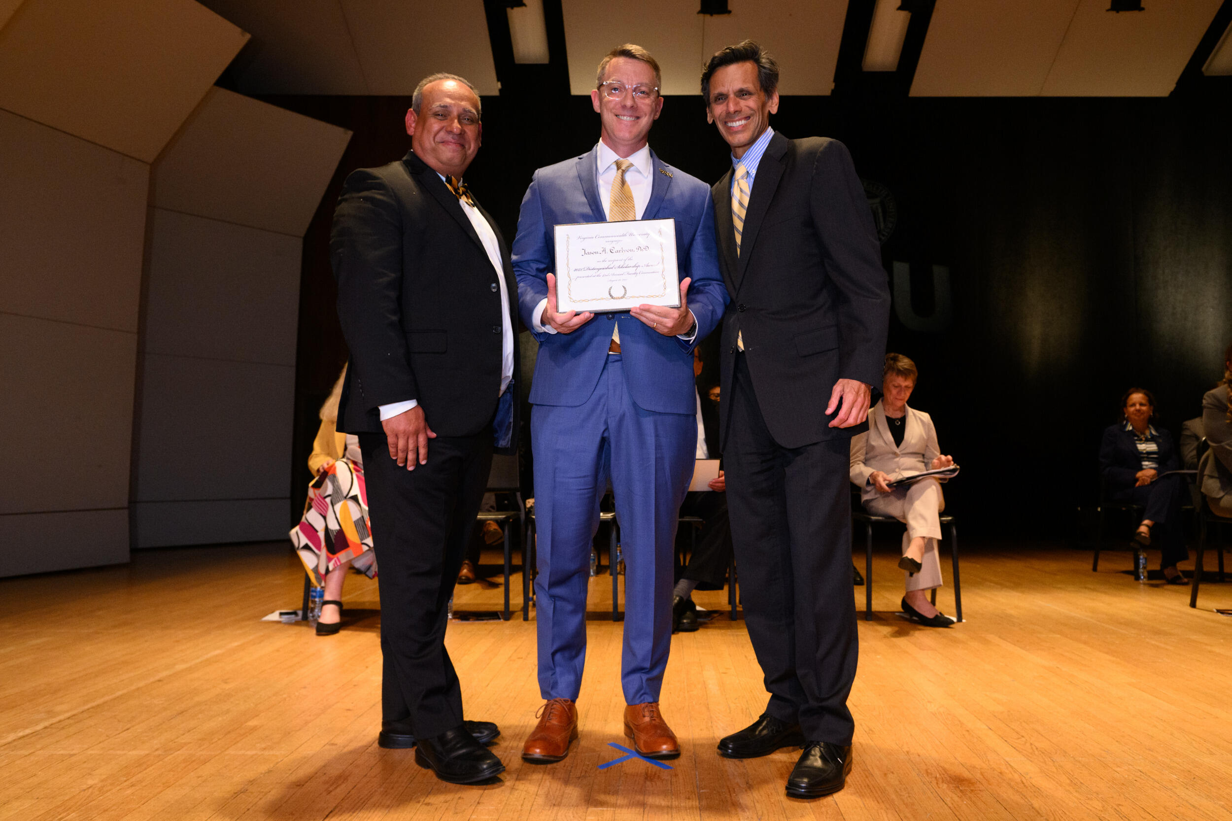 Three men in coats and tie smile. The man in the middle holds a piece of paper.