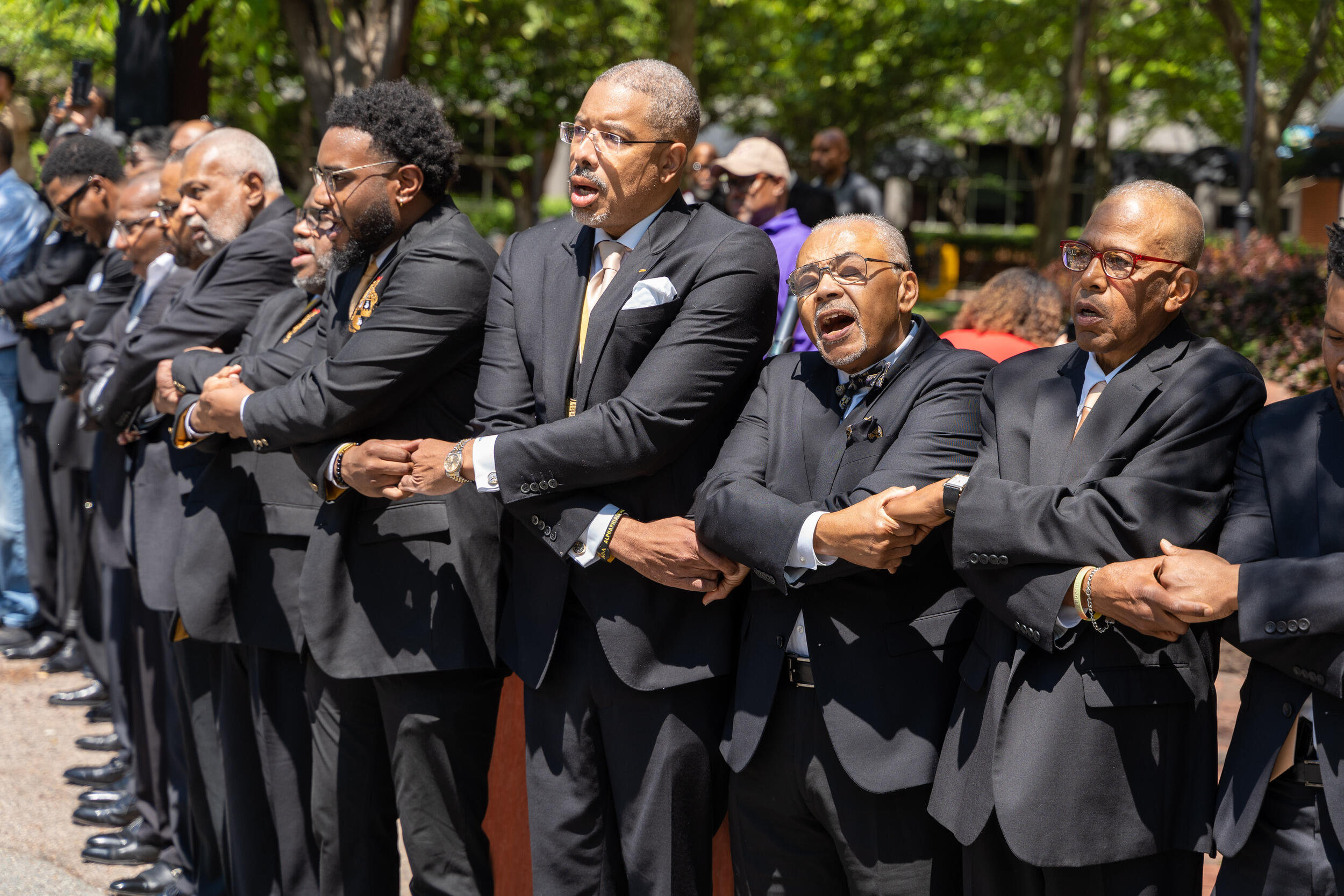 Men in black suits holding hands and singing. 