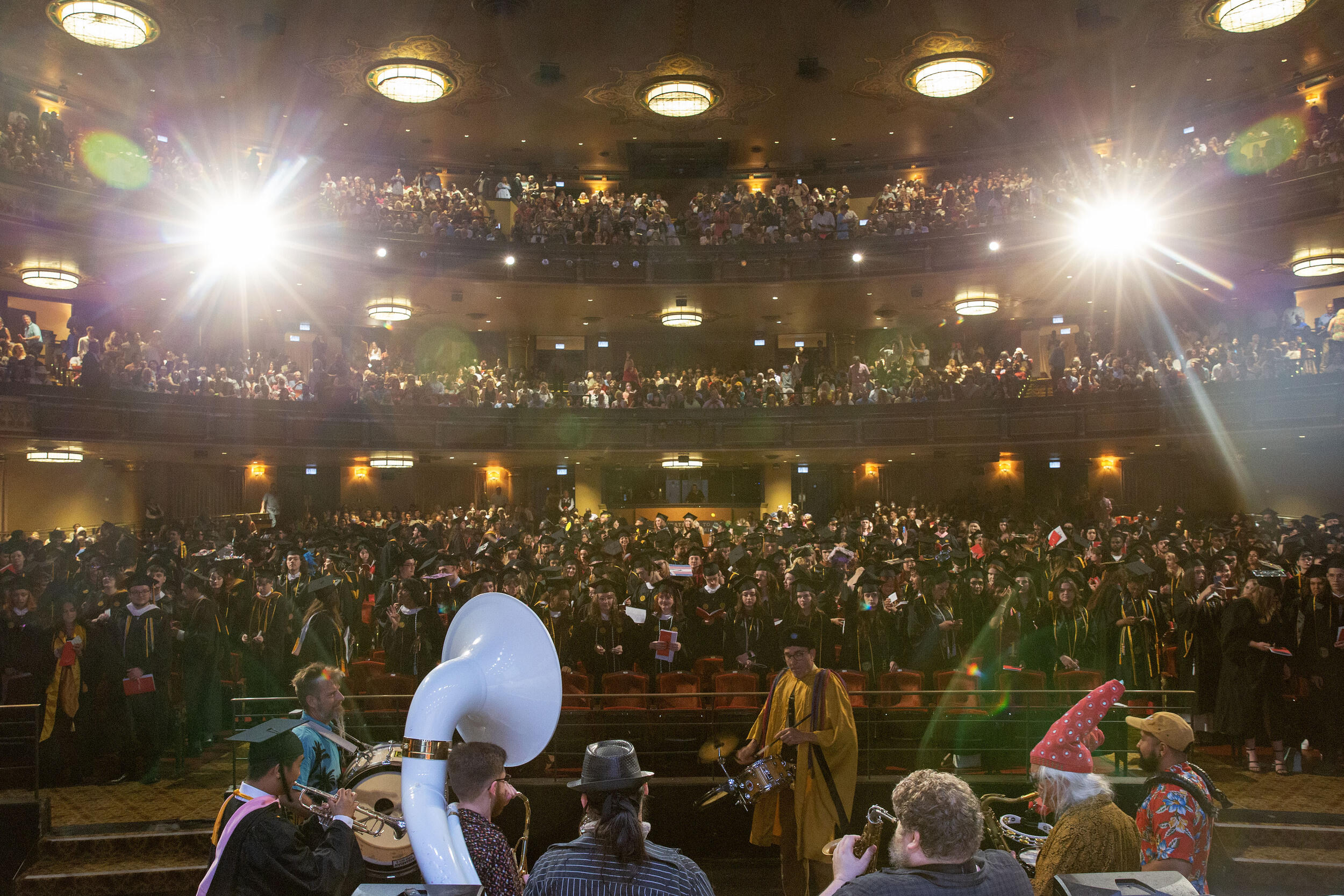 A photo of a theater from the view of the stage looking out at the audeince. The theater is filled with people standing. 