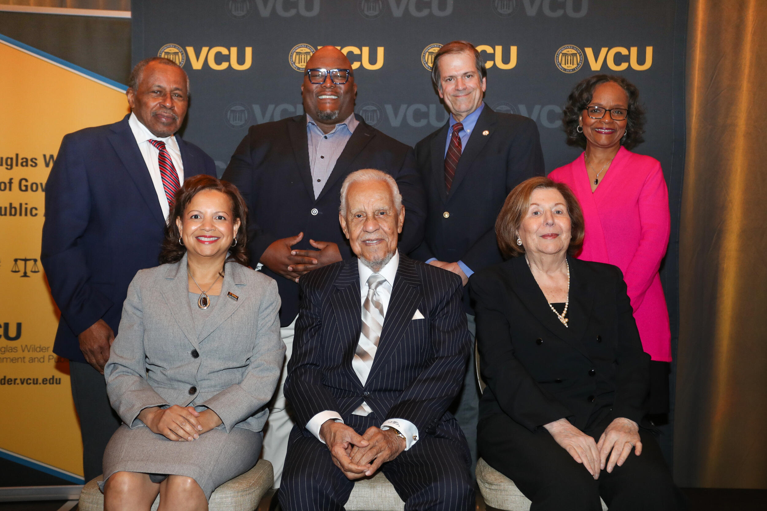 A photo of four people standing and three people sitting. 