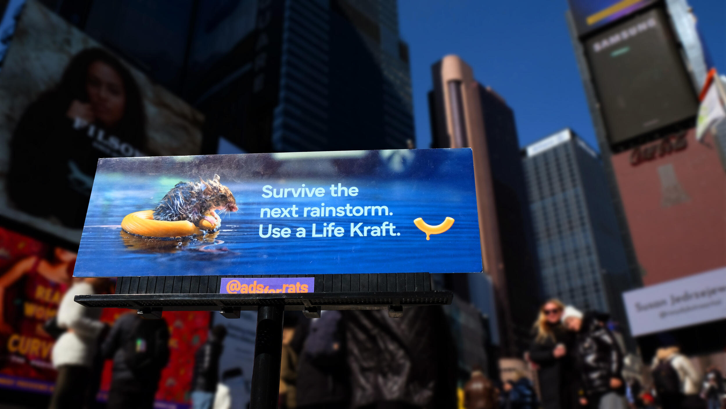 A photo of a small billboard with a photo of a rat using two macaroni noodles as a flotation device in water. White text reads \"Survive the next rainstorm. Use a Life Kraft.\" 