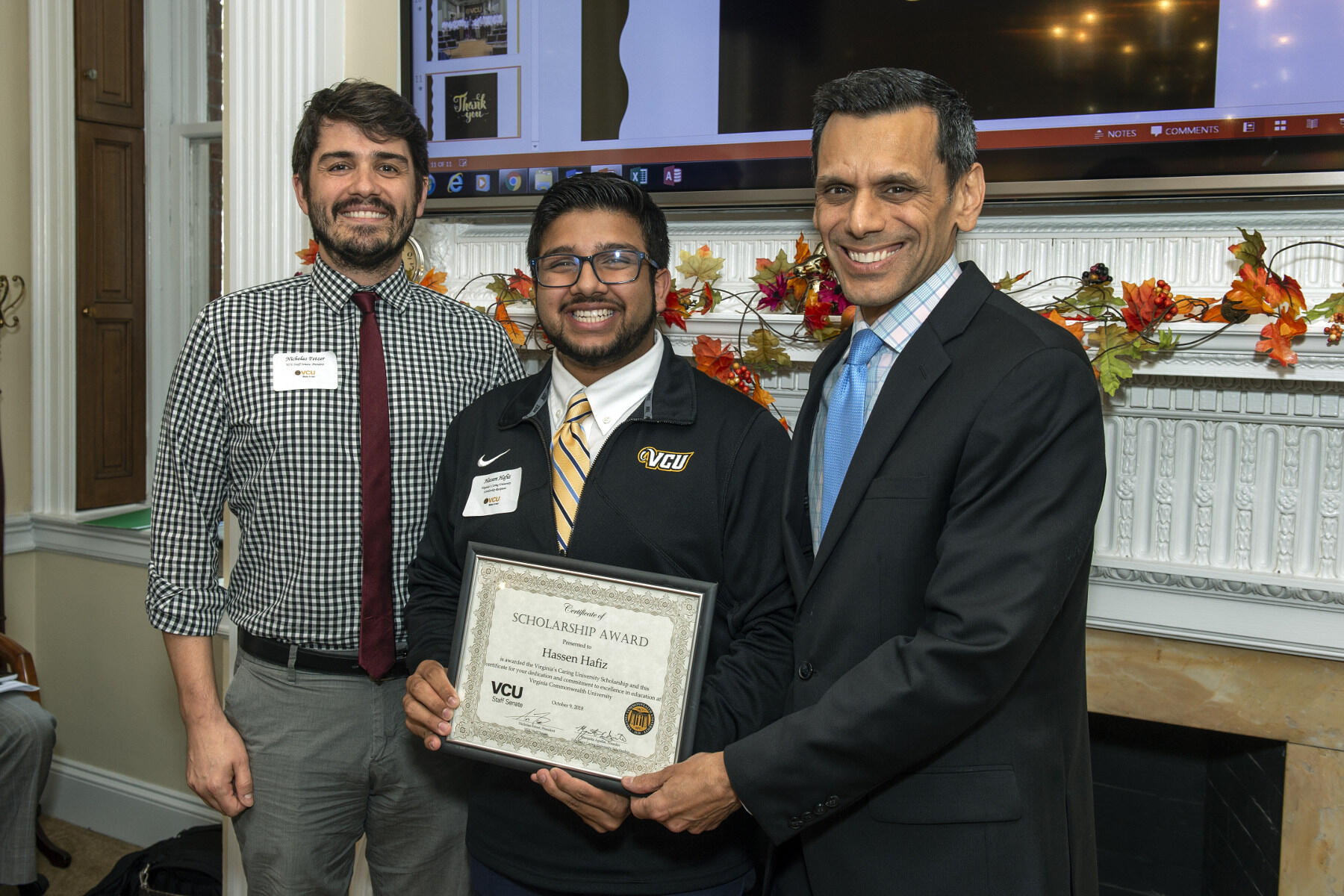 Three men in business clothes smiling and holding a certificate.