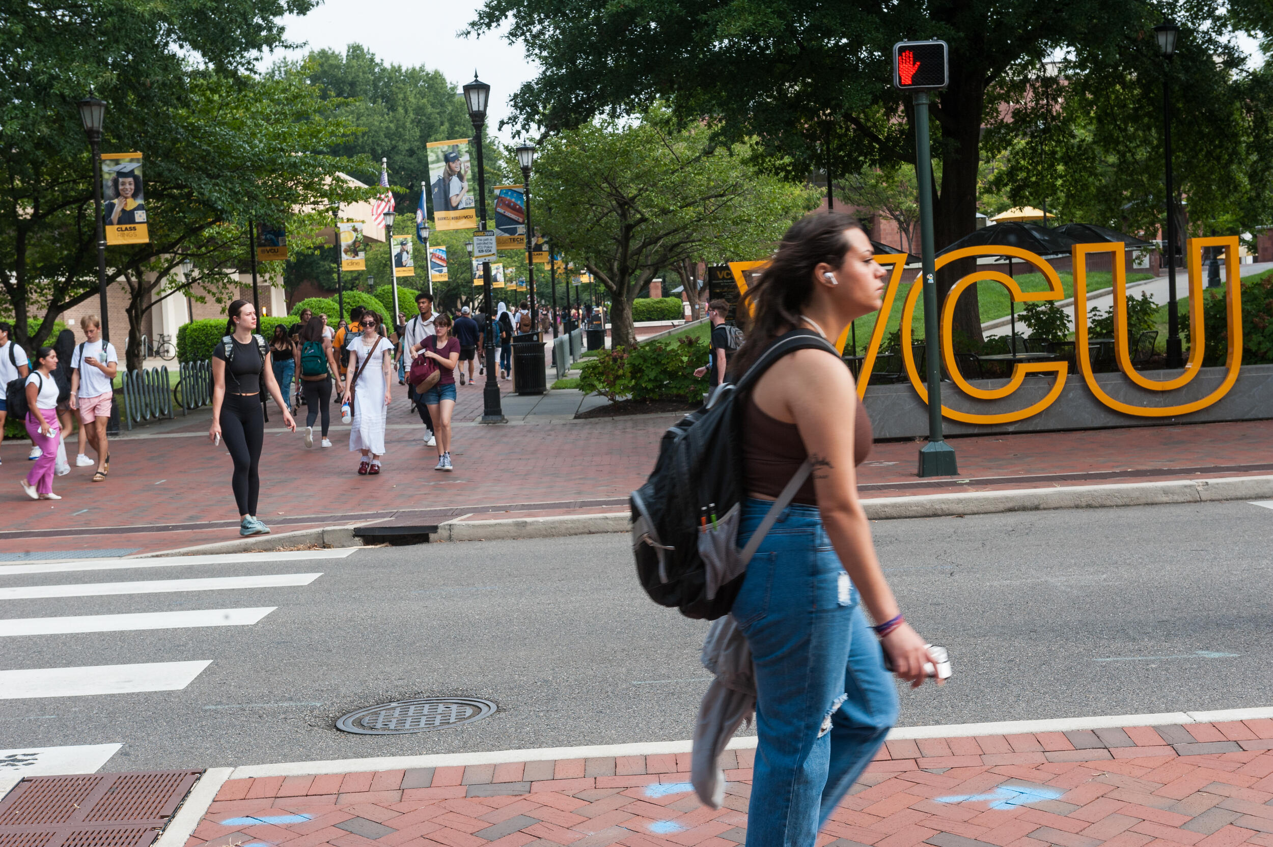 A person walking across the sidewalk. On the other side of the street is a sign that says \"VCU\"