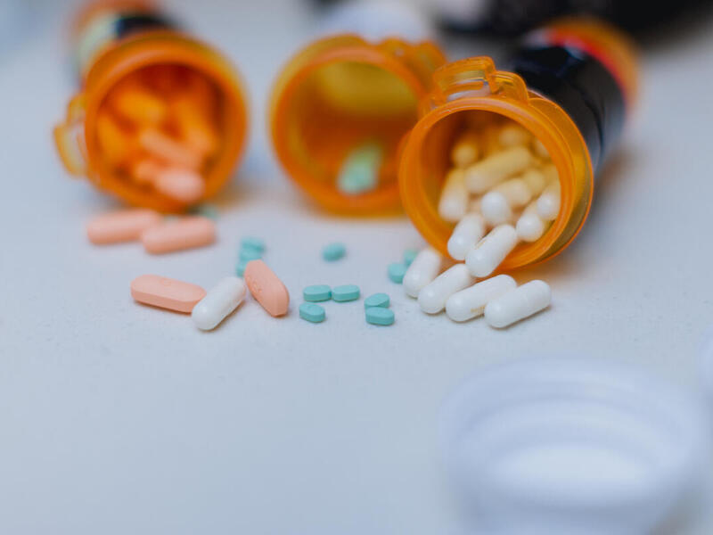 A photo of three orange pill bottles laying on their sides with pills spilling out from them. 