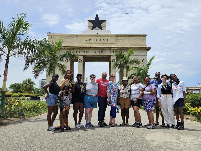 A photo of 12 people standing in front of an arch