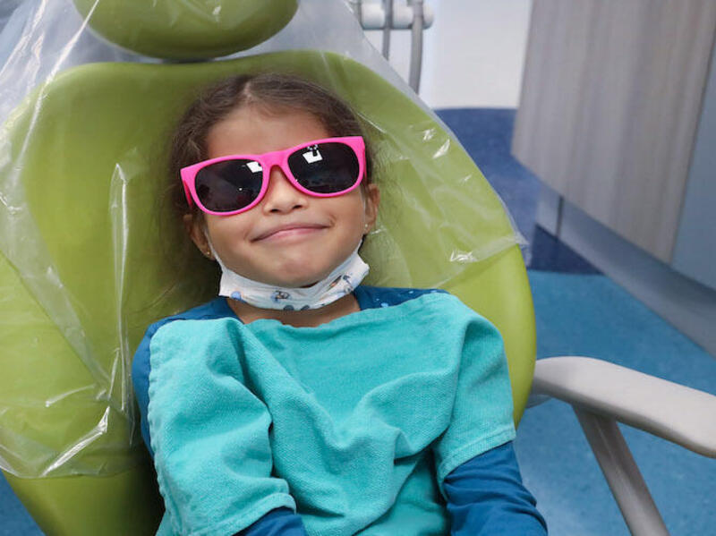 A child wearing pink sunglasses sitting in a dentist's chair. 