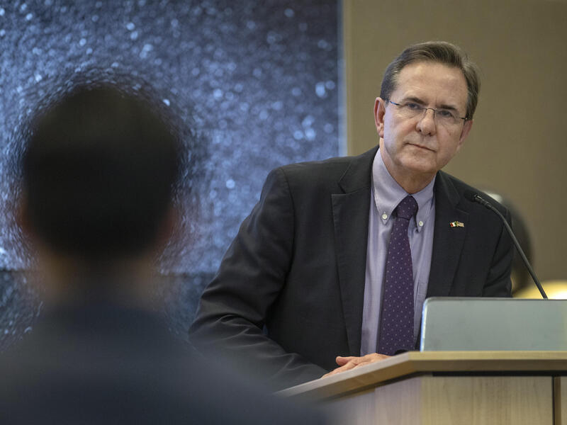A photo of a man standing at a podium looking at a person in front of him. 