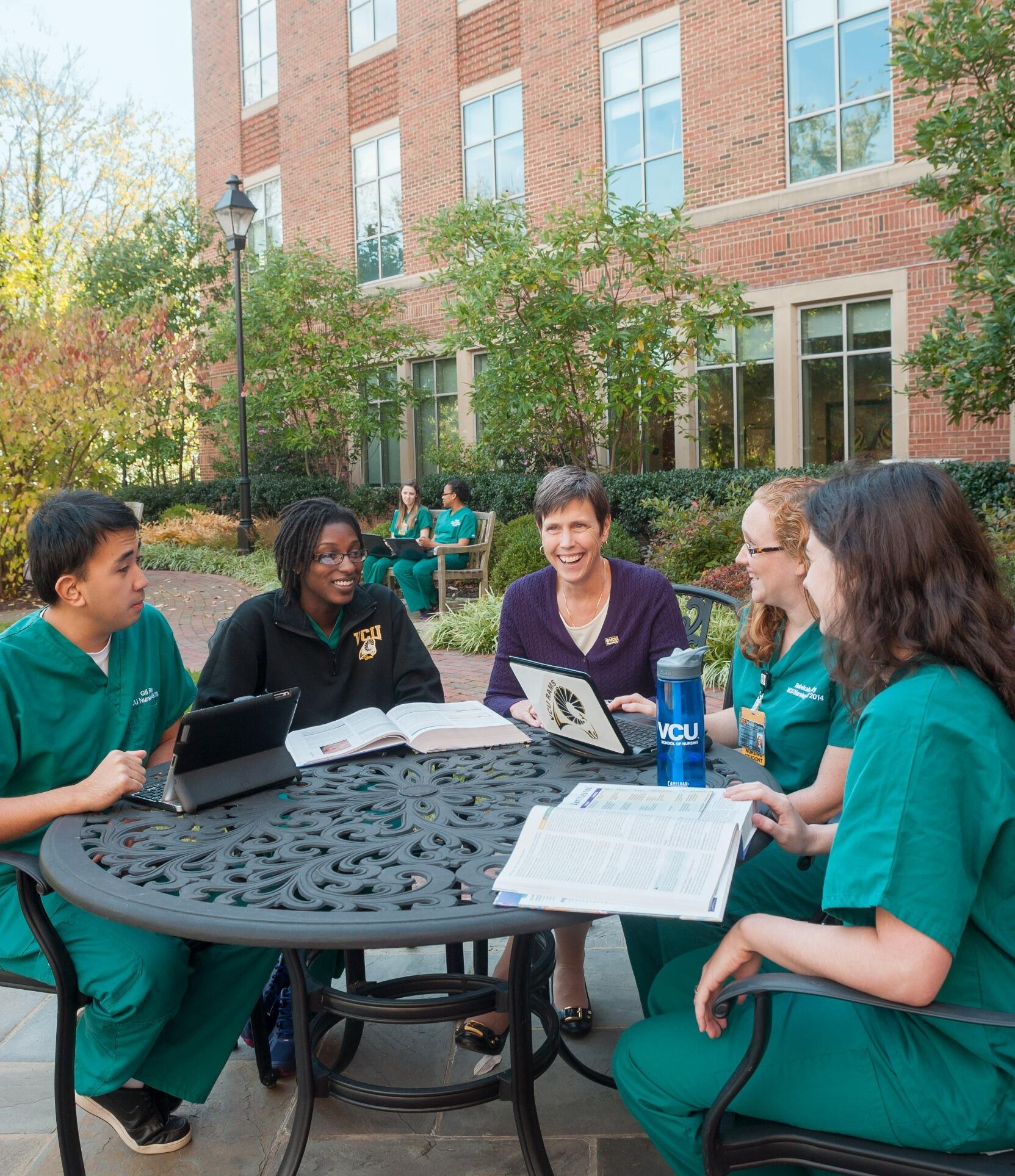 A photo of five people sitting around a table outside. 