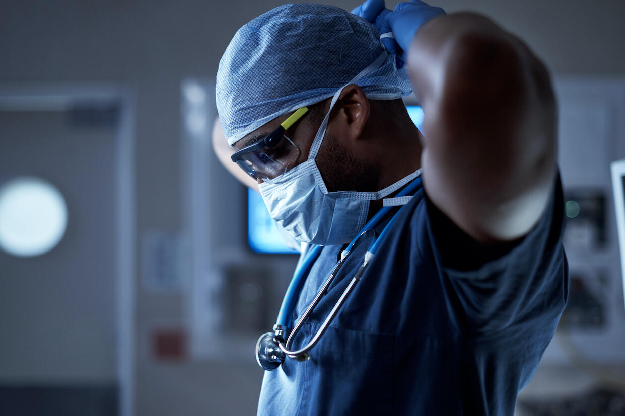 A physician in scrubs tying on surgical mask. 