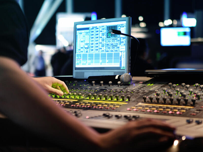 A photo of a person standing in front of sound mixing equipment. 