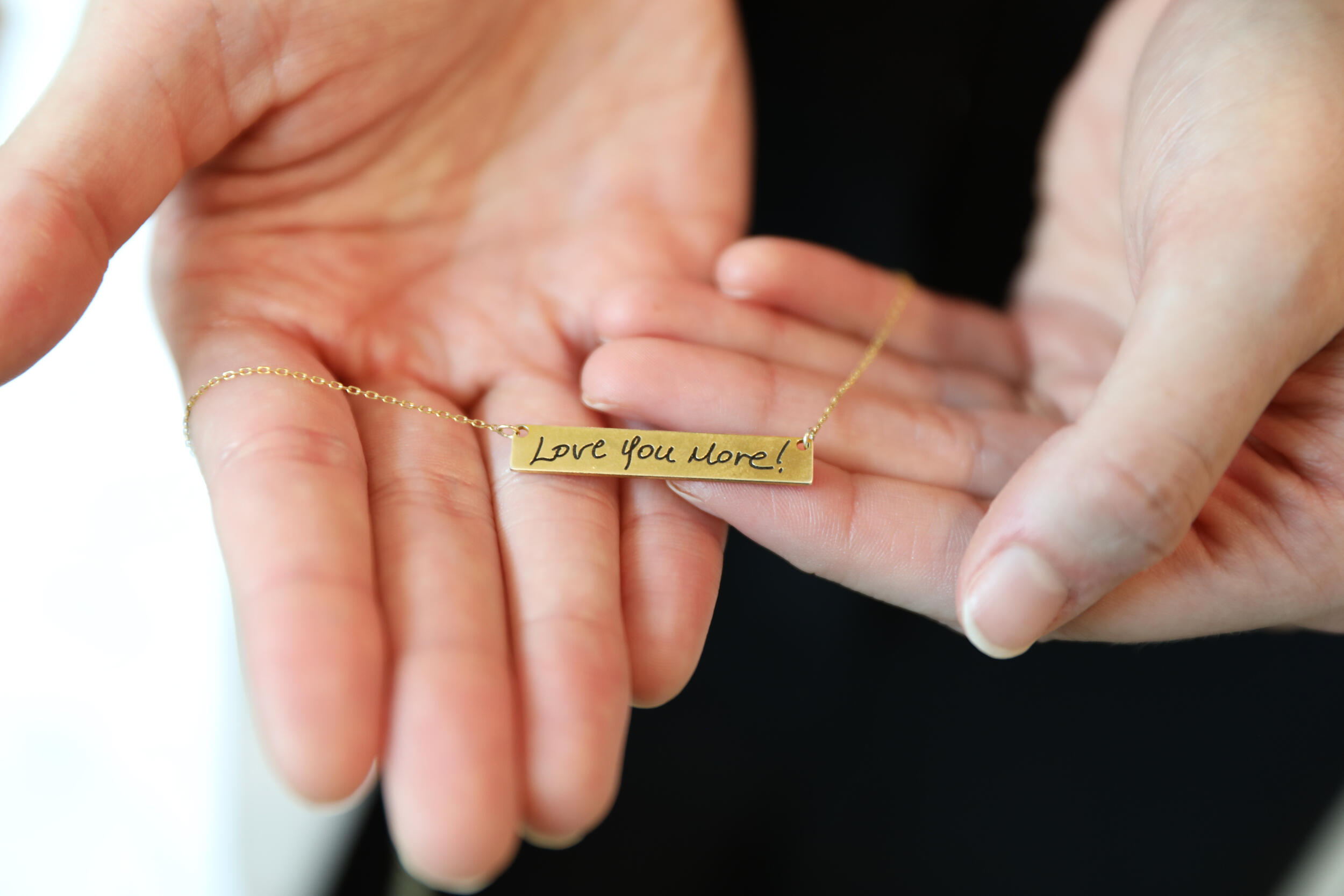 A photo of hands holding a necklace that says \"Lov You More!\"