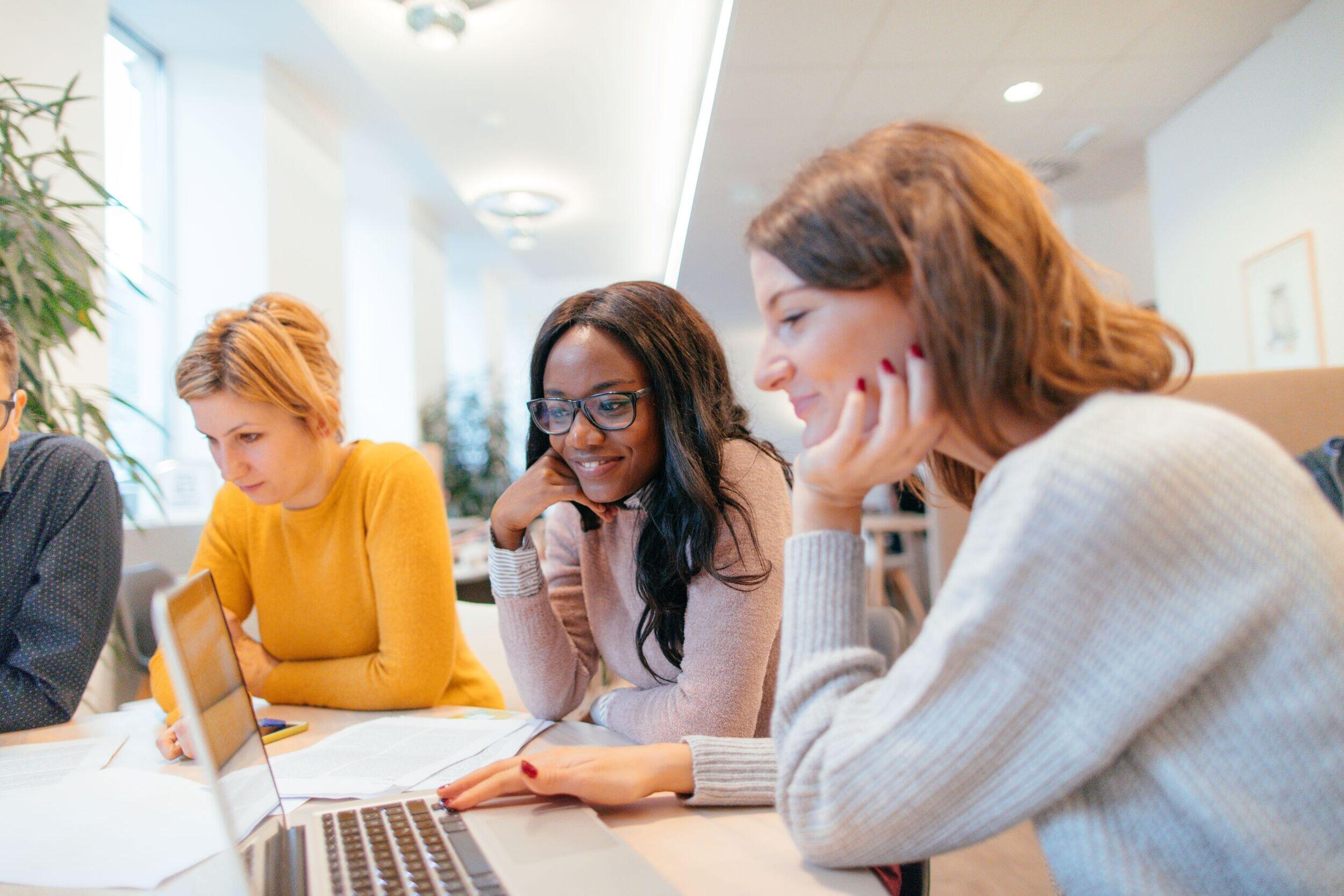 A group of workers around a table looking at tables and laptop screens.