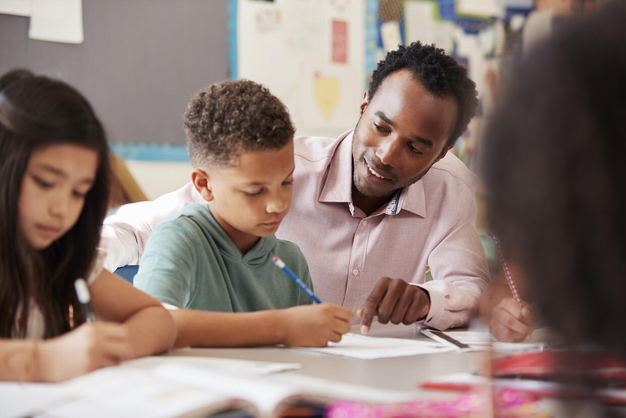 A teacher sits at a table to help elementary school students with their classwork.