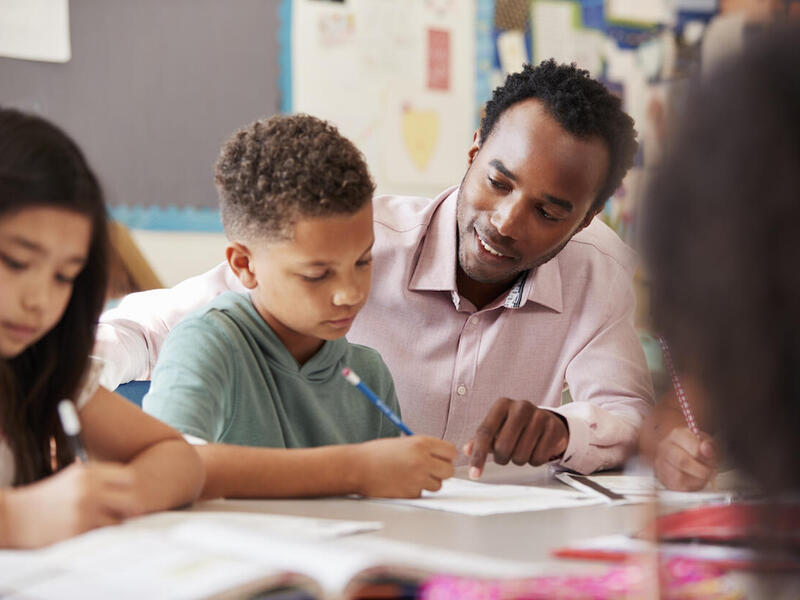 A teacher sits at a table to help elementary school students with their classwork.