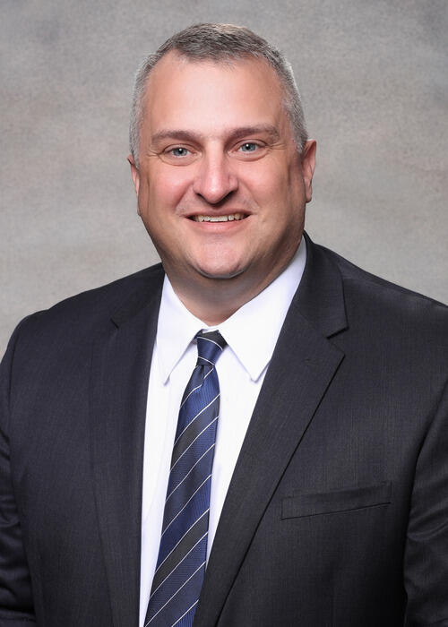 A photo of a man from the chest up. He is wearing a suit and tie. 