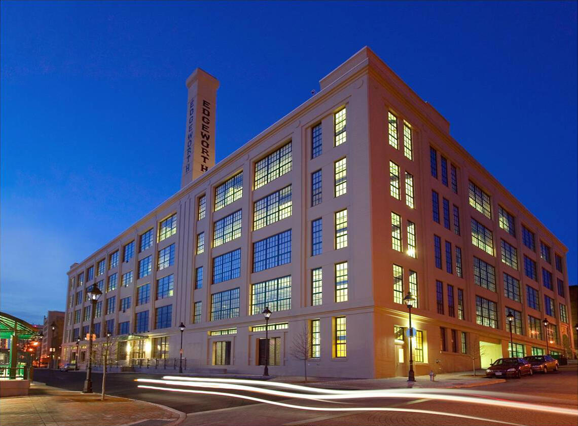 A large loft-style building in downtown Richmond is lit up at night with cars passing by.