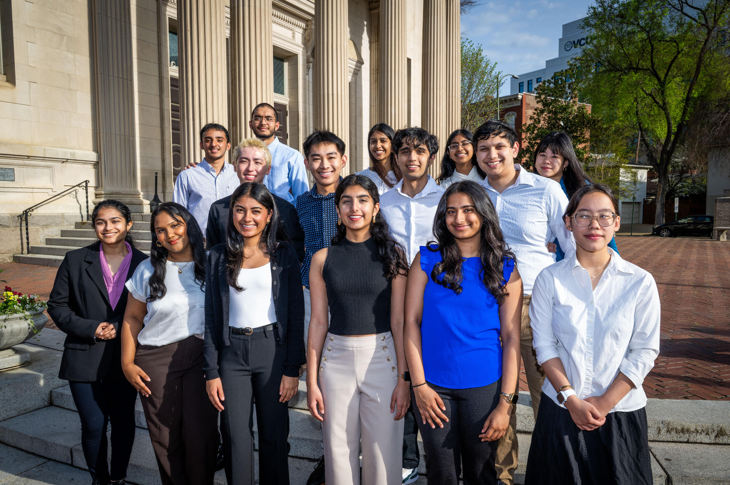 Rows of men and women stand outside in front of a building with columns.