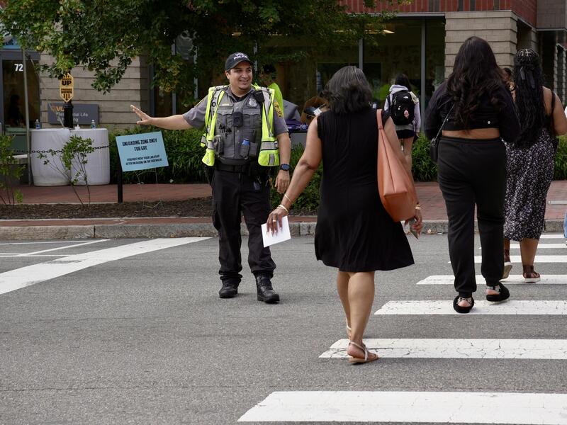 A photo of a police office wearing a yellow visability vest guiding people across a crosswalk. 