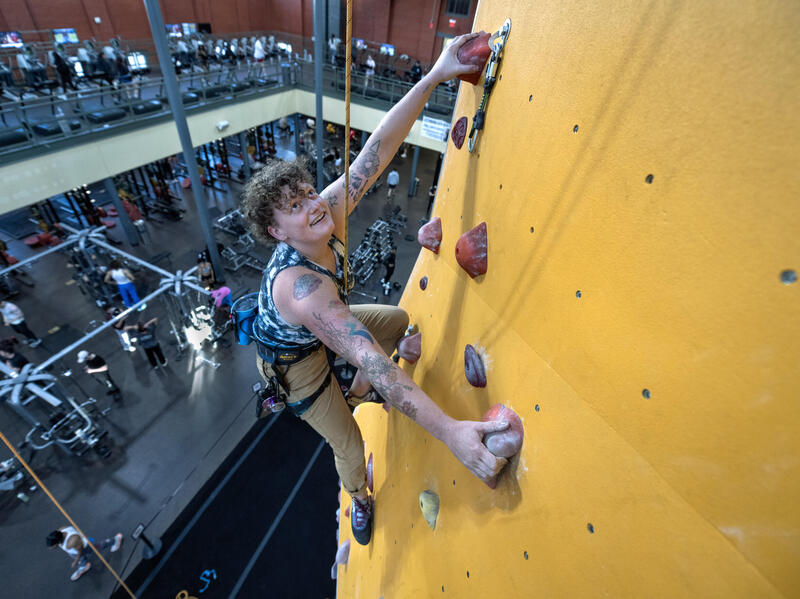 A photo of a person climbing up a yellow rock climbing wall. 