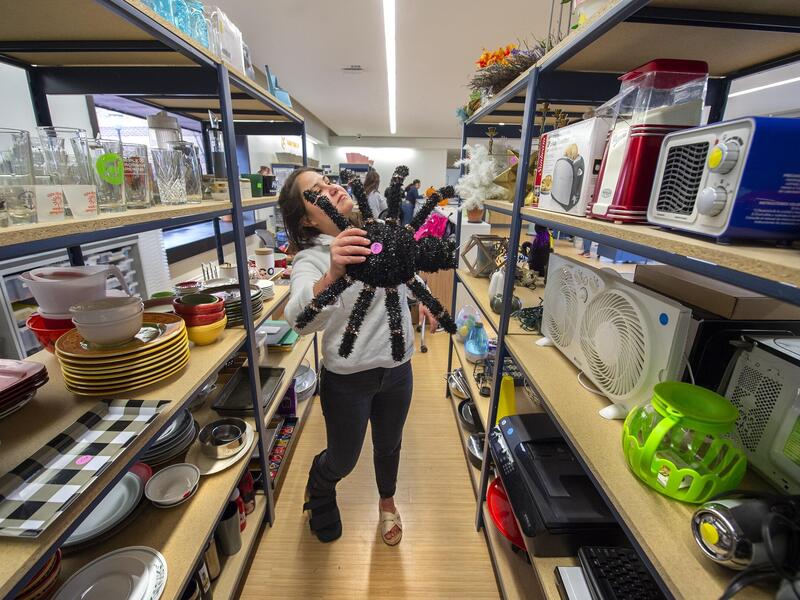 A photot of a woman in an isle between two shelving uinits holding a large fake spider. 