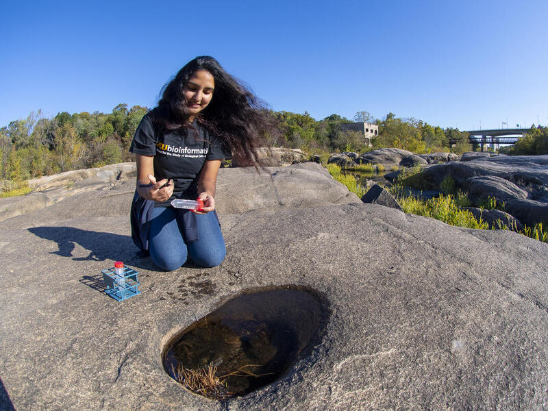 A student holding a water sample kit in front of a rock pool along the James River in Richmond, Virginia.