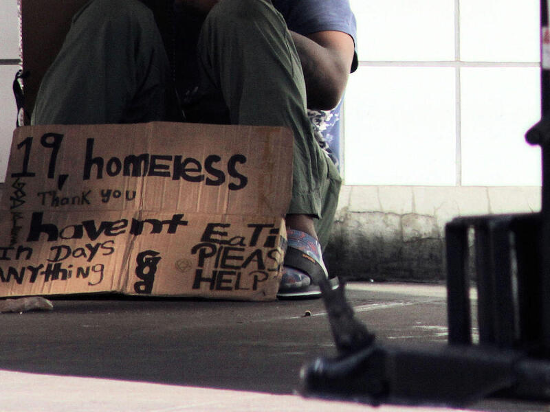 Homeless teenager sitting on the ground with a sign asking for help.