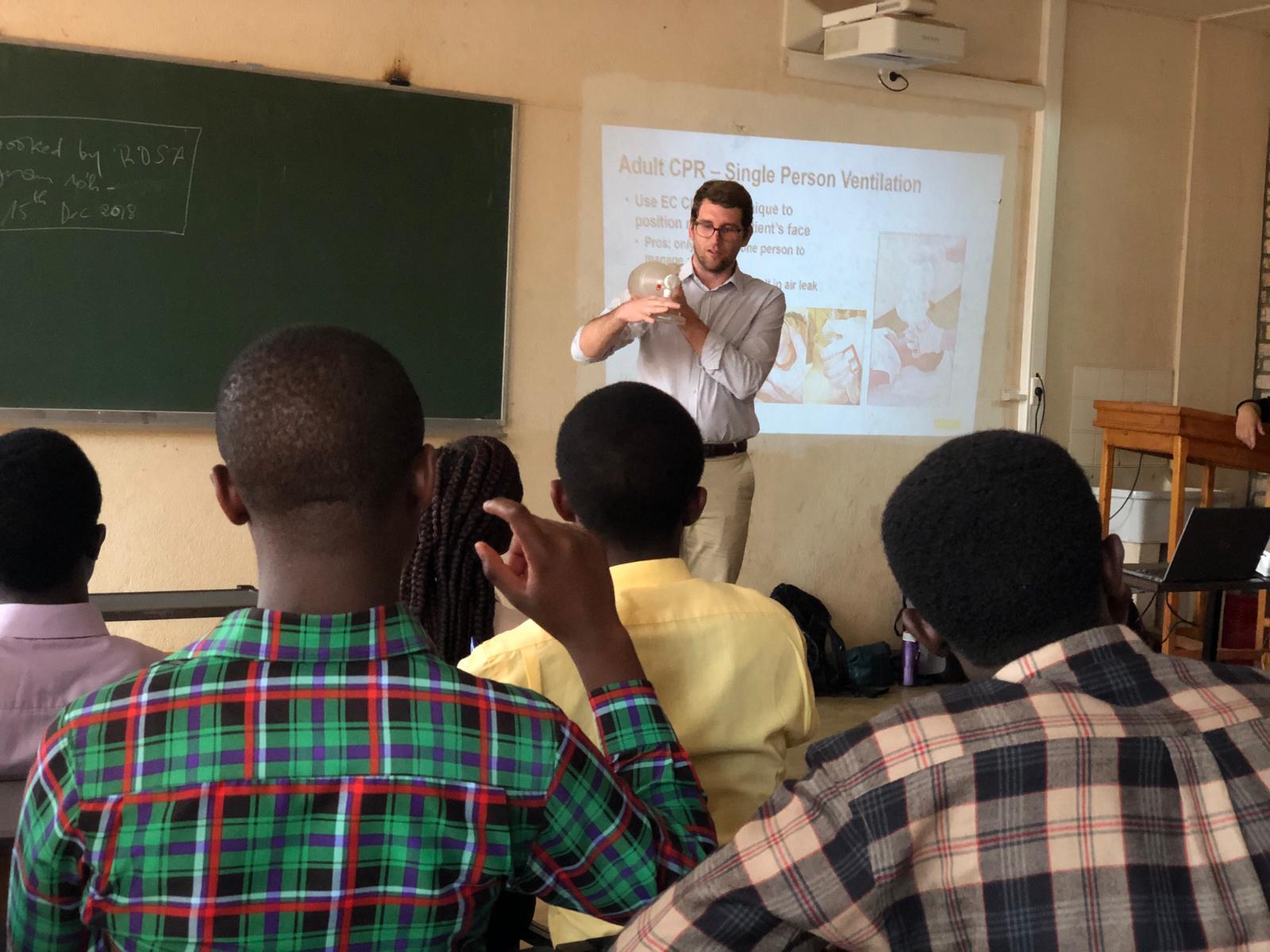 A person stands in front of a projector speaking to a seated group of people.