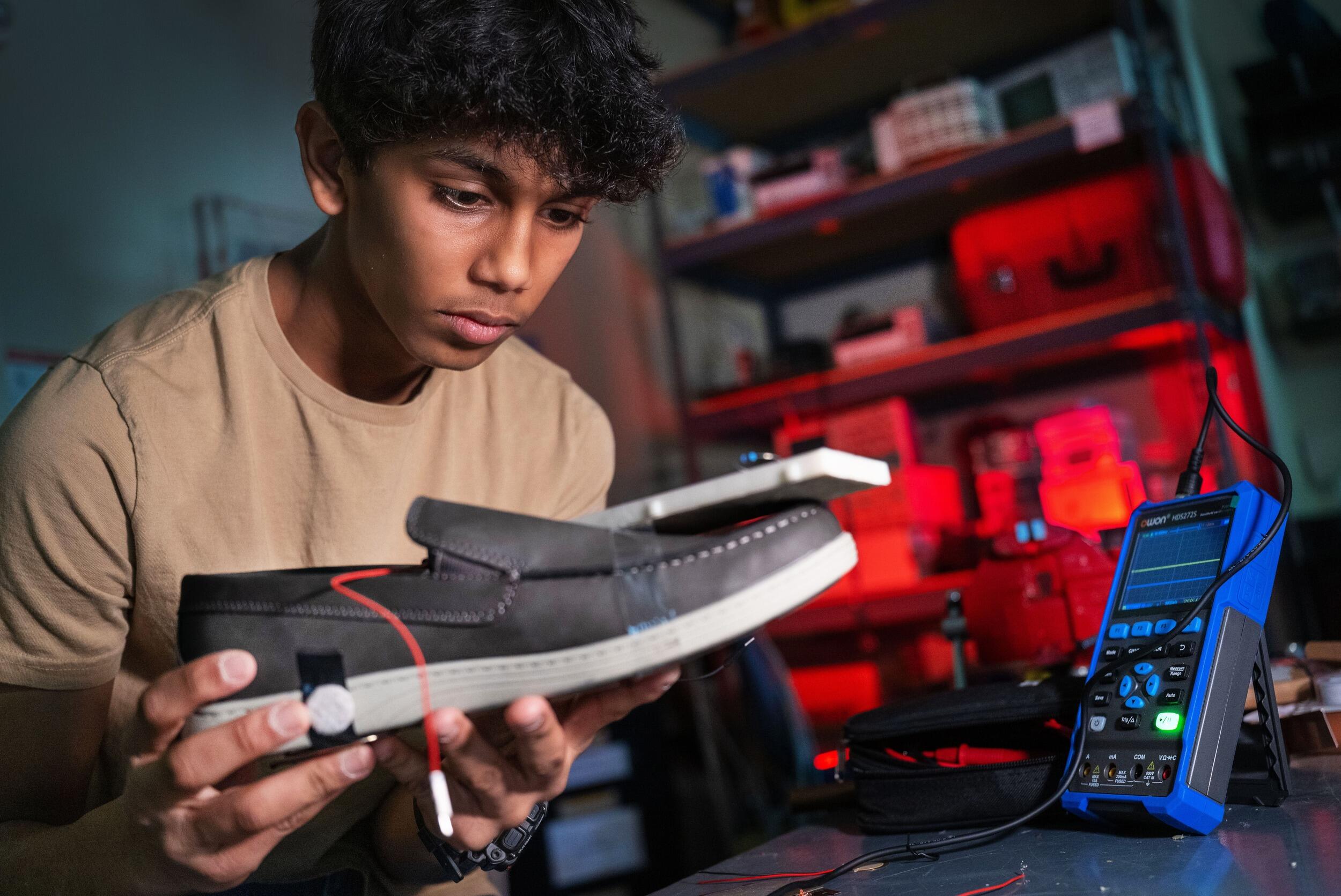 A photo of a teenage boy holding a shoe with a wire on it. 
