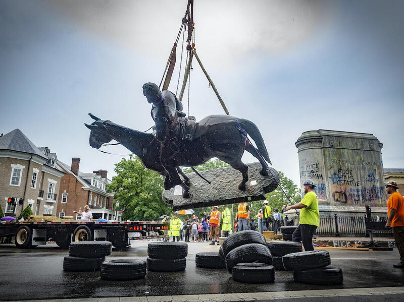 A statue is being placed on the bed of a truck by a crane.