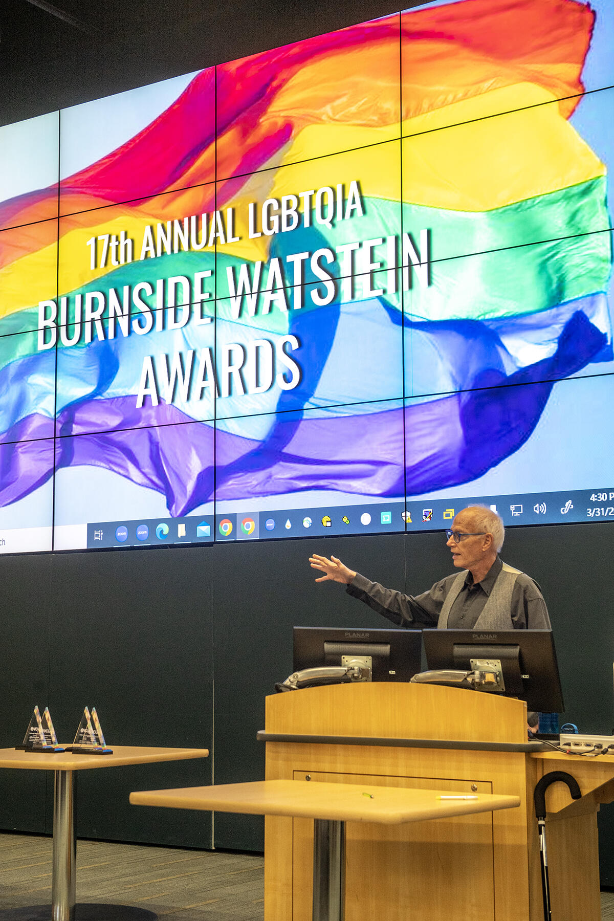 A man speaking at a podium with his left arm outstretched. 