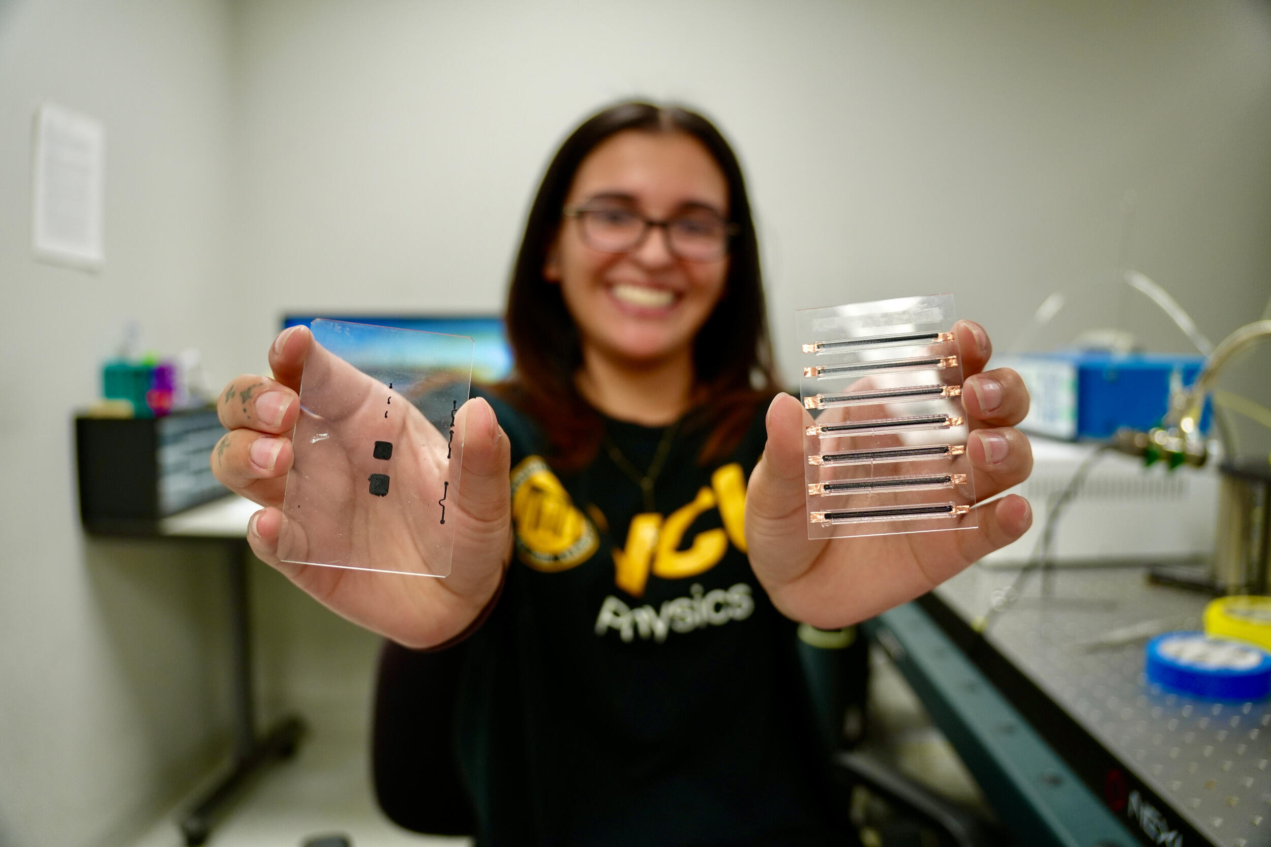 A woman in glasses smiles and holds up a 3D printed material to the camera.