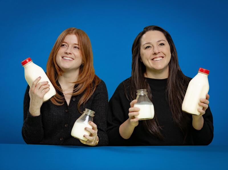 Two women wearing black shirts holding a container of milk in each hand